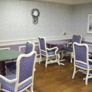A cozy dining area with blue upholstered chairs and wooden tables, adorned with a decorative wall clock.