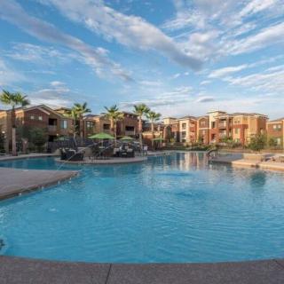 A serene view of a luxurious resort pool surrounded by palm trees under a partly cloudy sky.