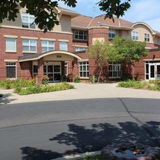 A brick building with an arched entrance surrounded by greenery and adjacent to a paved road.