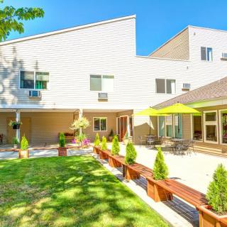 A modern home with a spacious backyard and patio area, featuring outdoor seating and lush landscaping on a sunny day.
