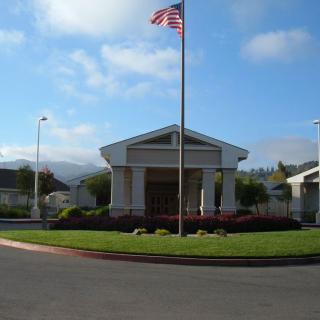 A building with an American flag on a pole, surrounded by a well-maintained lawn under a clear sky.
