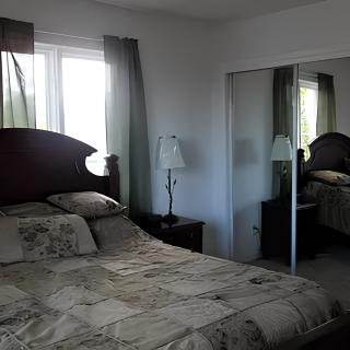 A cozy bedroom with a bed, bedside lamp, and mirrored closet doors.