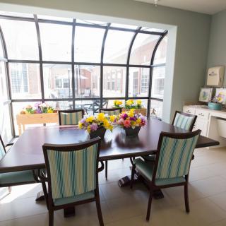 A bright dining room with a large window, decorated with colorful flowers on the wooden table.
