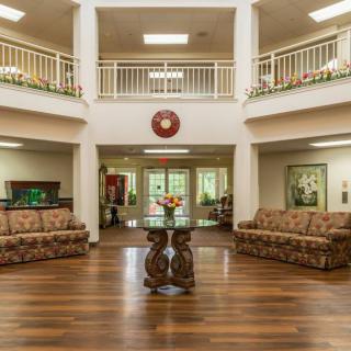 A well-decorated lobby with sofas and a central table, featuring wooden flooring and an upper balcony.