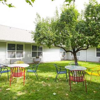 A serene outdoor patio with colorful chairs and tables set on a lush green lawn under a tree.