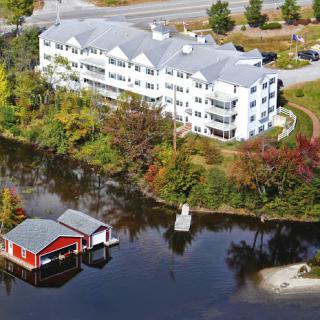 A picturesque aerial view of a residential building by a serene waterfront, surrounded by autumn foliage.
