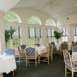 A bright and elegant restaurant dining area with neatly arranged tables and chairs, enhanced by natural light and greenery.