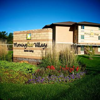 A well-maintained apartment complex with lush landscaping and a prominent sign in front.