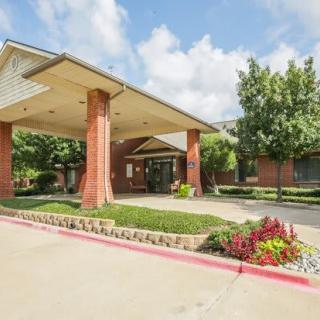 An entrance to a building with a covered driveway, surrounded by well-maintained landscaping and colorful flowers.