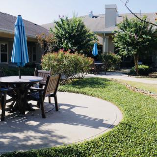 A sunny garden patio with tables, chairs, and umbrellas surrounded by greenery.