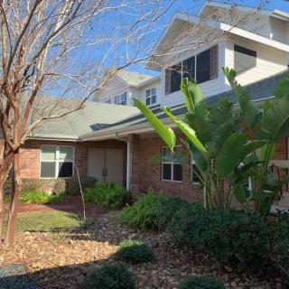 A brick residential house with landscaped garden and trees on a sunny day.