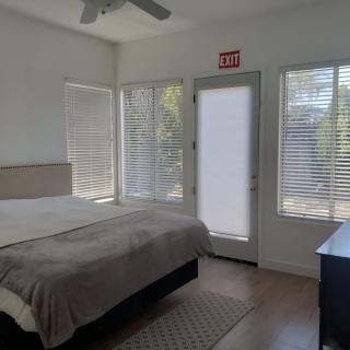 A minimalist bedroom with a bed, dresser, and large windows with blinds.