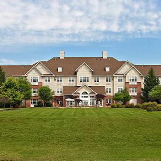 A large residential building with a spacious lawn and trees under a partly cloudy sky.