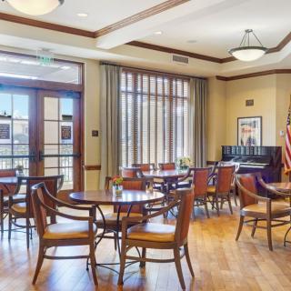 A well-lit room with wooden floors, featuring tables and chairs arranged for a meeting or gathering.