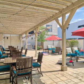 A spacious outdoor patio with comfortable seating under a wooden pergola, featuring tables, chairs, and colorful umbrellas.