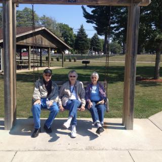 Three people sitting on a swing in a park setting.