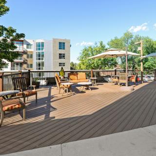 A spacious outdoor patio area with seating and umbrellas, adjacent to apartment buildings on a sunny day.