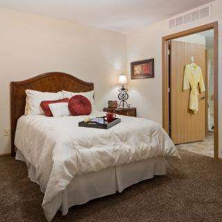 A cozy bedroom with a neatly made bed, bedside lamp, and elegant decor.