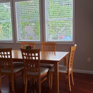 A cozy dining area featuring a wooden table set with six matching chairs and large windows with blinds.