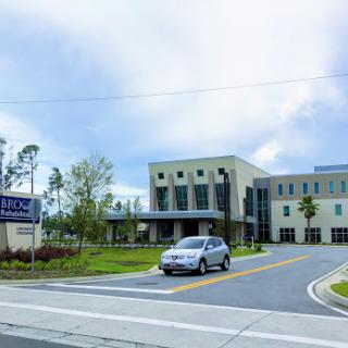 A modern medical facility with a car driving by under a cloudy sky.
