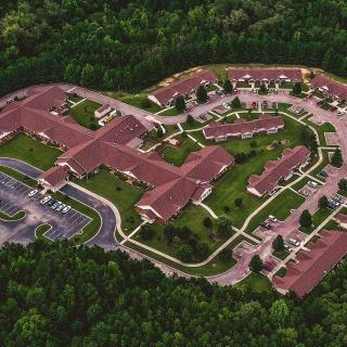 Aerial view of a large complex with red-roofed buildings surrounded by greenery and connected by roads.