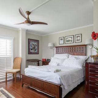 A cozy and elegantly designed bedroom featuring a wooden bed, stylish ceiling fan, and tasteful decor.