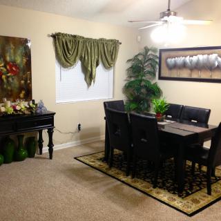 A cozy dining room featuring a table set with chairs, lush plants, decorative artwork, and elegant window drapes.
