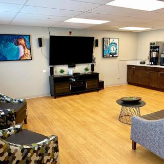 A modern lounge area with a television, comfortable seating, artwork on the walls, and a coffee station.