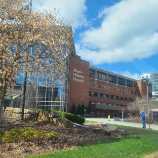 A modern building surrounded by greenery and blue skies, with a person walking on the pathway.