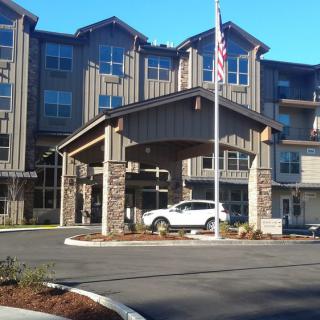 A modern building entrance with a car parked under the portico and an American flag flying nearby.