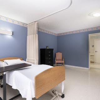 A clean and well-lit hospital patient room featuring a bed, curtains, and a dresser.