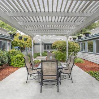 A modern outdoor patio with a pergola and dining set surrounded by well-maintained garden landscaping.