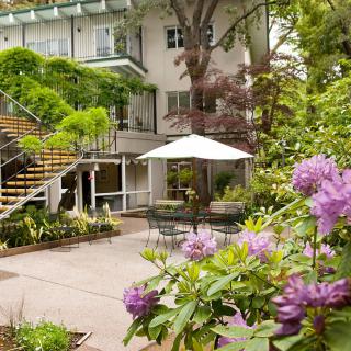 A charming garden patio with vibrant flowers and comfortable outdoor seating under an umbrella.