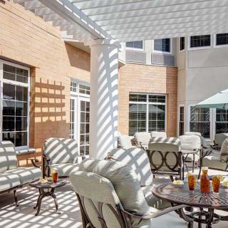 A sunny patio with comfortable seating and tables under a pergola.