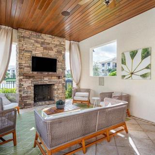 A stylish outdoor living space featuring a cozy seating area, stone fireplace, and television, all under a wood-paneled ceiling.