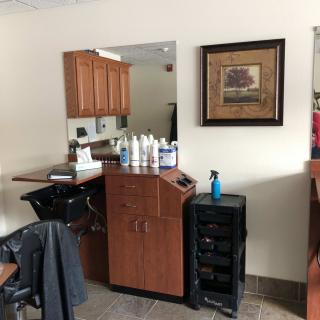 A hair salon interior featuring a styling station with various products, a mirror, and a framed picture on the wall.
