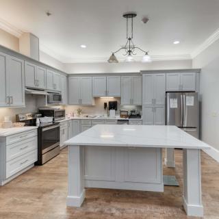 A spacious and modern kitchen featuring gray cabinets, a large island counter, stainless steel appliances, and elegant overhead lighting against wood flooring.
