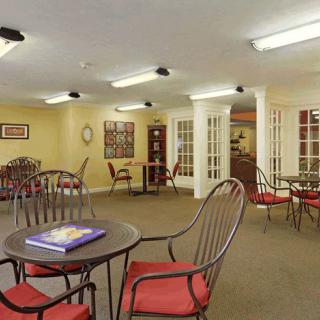 A cozy room with red cushioned chairs and round tables, well-lit by overhead lights.