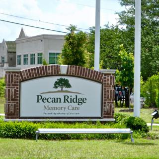 A sign for Pecan Ridge Memory Care in front of a building.