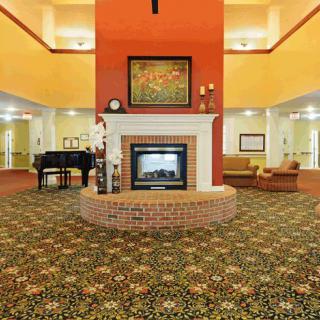 A spacious hotel lobby featuring a central fireplace, a grand piano, and comfortable seating areas.