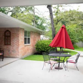 A cozy patio setup with a red umbrella, table, and chairs in a backyard.