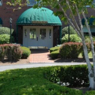 A building entrance with a green canopy, surrounded by well-maintained landscaping and a brick pathway.