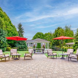 A beautiful garden patio with chairs and umbrellas overlooking a gazebo.