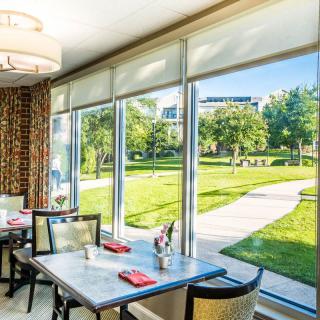 A cozy restaurant interior with a scenic view of a lush, green outdoor area through large windows.