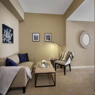 A cozy living room with a beige color scheme, featuring a sofa, armchair, coffee table, and decorated with wall art and a mirror.