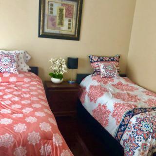 A cozy bedroom featuring two twin beds with floral patterned bedding, separated by a nightstand and adorned with wall art.