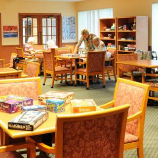 A cozy community center room with tables, chairs, and board games, where seniors are engaged in activities.