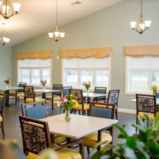 A bright and inviting dining room with neatly arranged tables and chairs, illuminated by chandeliers.