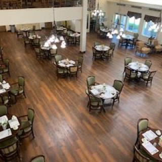 A spacious dining room with elegantly set tables and chairs on a wooden floor.
