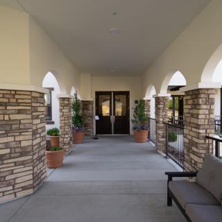 A covered entrance with stone pillars and arched windows, featuring a bench and potted plants.
